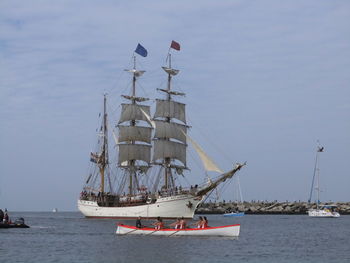 Women rowing boat by ship in sea against sky