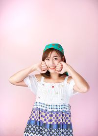 Portrait of smiling woman touching cheeks against pink background