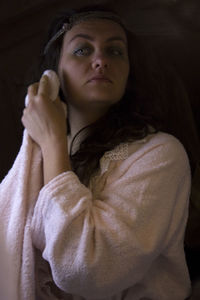 Woman wiping face with towel while standing against black background