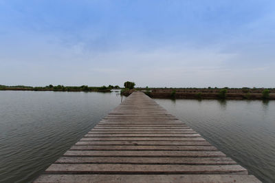 Wooden jetty over river against sky