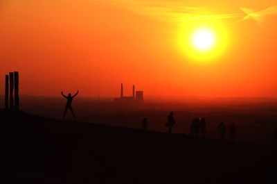 Silhouette people standing on land against orange sky