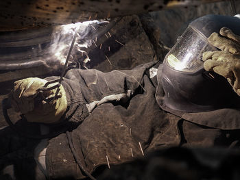 A gas electric welder in a welding mask is welding the joint of a gas pipe.