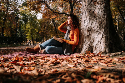 Woman sitting on tree trunk during autumn