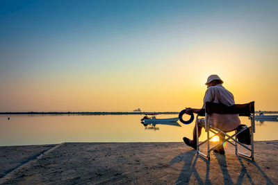 Rear view of man on sea against sky during sunset