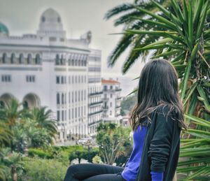 Rear view of woman with palm trees against buildings