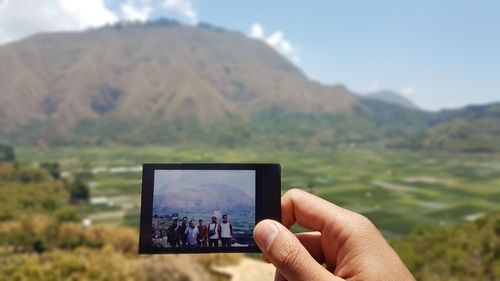 Cropped hand holding photograph against mountains