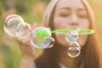 Close-up of young woman blowing bubbles during sunny day at public park