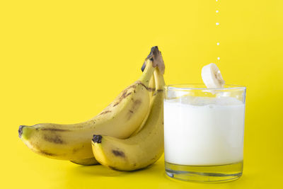 Close-up of drink in glass by banana against yellow background