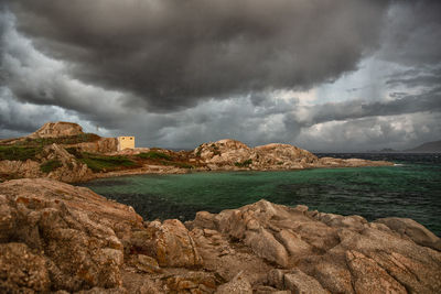 Scenic view of sea and rocks against storm clouds