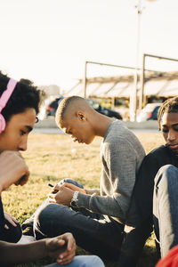 Male friends sitting on field during sunny day