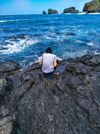 Rear view of woman sitting on rock in sea