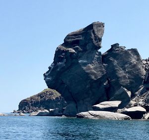 Rock formation in sea against clear blue sky