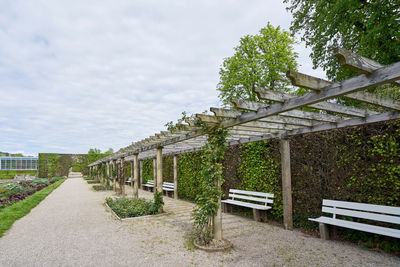 Empty bench by footpath in park against sky