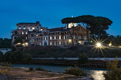 Illuminated old building by tiber river against sky at dusk