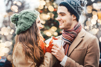 Close-up of smiling couple holding coffee cup during winter