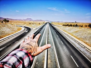 Cropped tattooed hand of man gesturing on road against sky