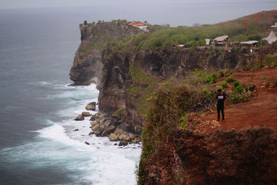 Rear view of woman standing on rock by sea