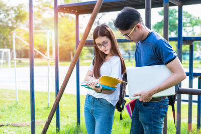University students reading book while standing at park