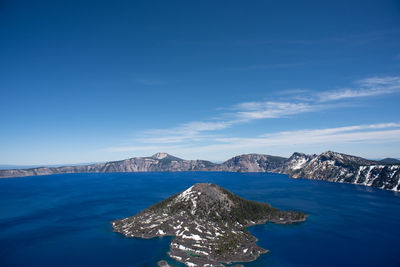 Scenic view of sea by mountains against blue sky