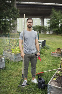 Full length portrait of mid adult man with rake and trowel in urban garden