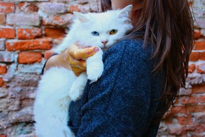 Full length of woman holding cat against brick wall