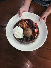 High angle view of person holding ice cream in plate on table