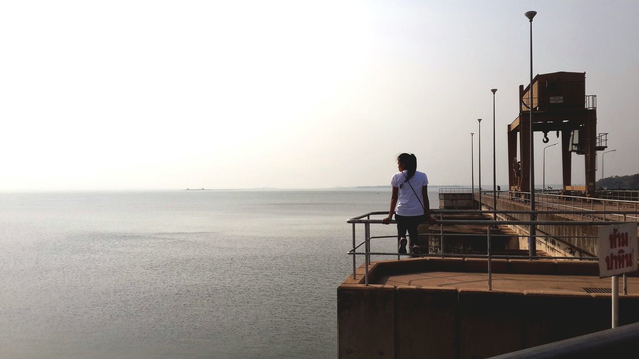 sea, horizon over water, clear sky, copy space, water, rear view, railing, lifestyles, full length, leisure activity, men, sitting, sky, pier, beach, person, standing, tranquil scene