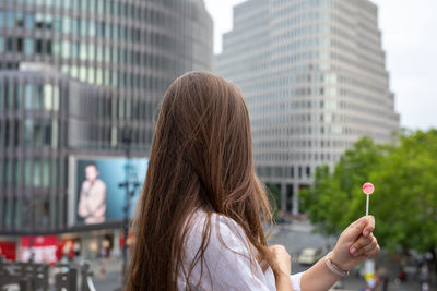 Side view of young woman holding lollipop by buildings in city
