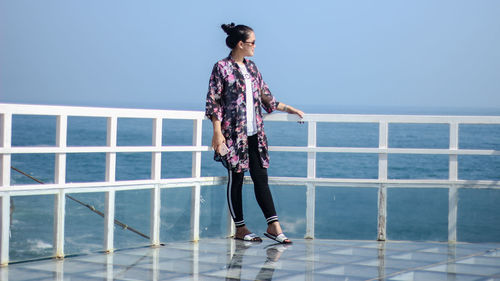Full length of woman standing by railing against sea