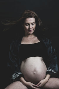 Pregnant woman sitting against black background