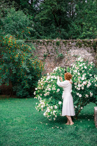 Full length of woman standing in park in blossoming bush