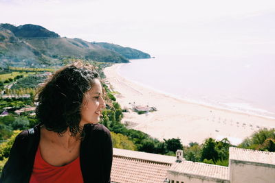 Young woman standing on mountain against sky during sunny day