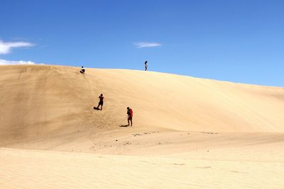 People on sand dune in desert against sky