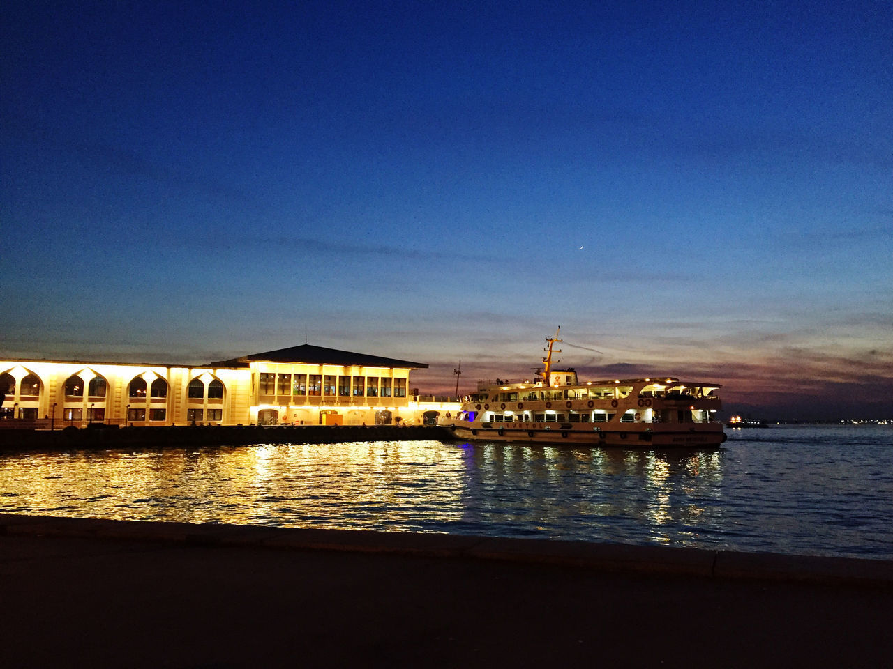 ILLUMINATED BUILDINGS BY SEA AGAINST BLUE SKY