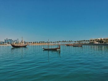 Boats sailing in sea against clear blue sky