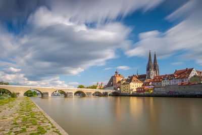 Arch bridge over river amidst buildings against sky