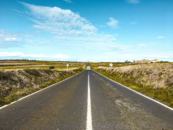Empty road amidst field against sky