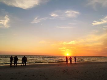 Silhouette people standing on beach against sky during sunset