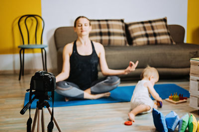 Young mother fitness instructor personal trainer record video near camera at home with baby