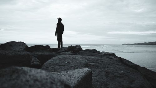 Man standing on rock by sea against sky