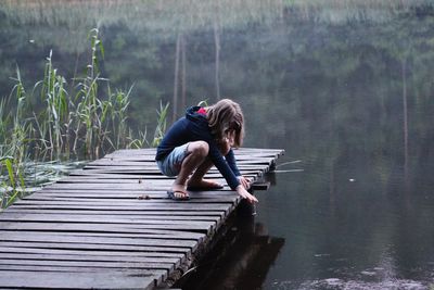 Teenager crouching on jetty over lake