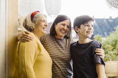 Happy woman with arms around son and mother-in-law while standing in balcony