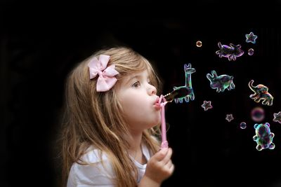 Side view of cute girl blowing animal shape bubbles against black background