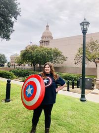 Portrait of smiling young woman with shield standing against built structure