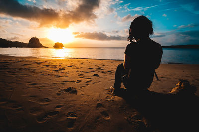 Rear view of woman looking at sea against sunset sky at a beach