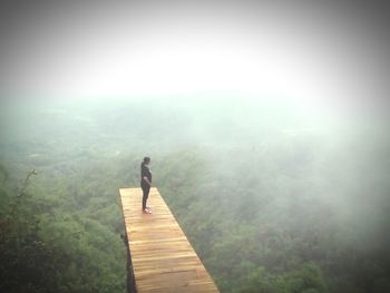 Man standing on mountain in forest during foggy weather