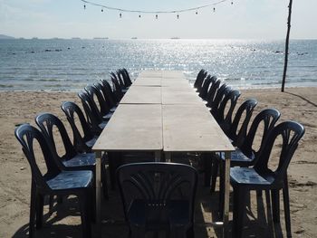 Empty chairs and tables on beach against sky