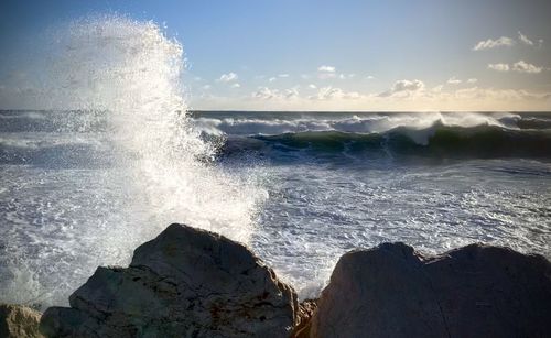 Waves splashing on rocks against sky