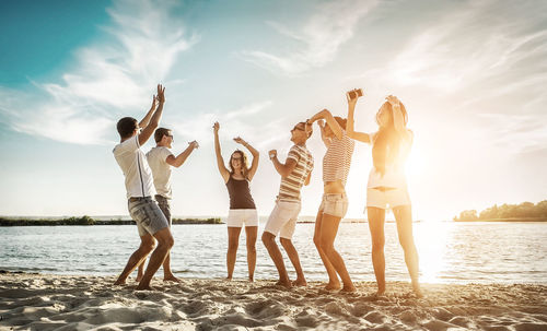 Rear view of friends standing at beach against sky