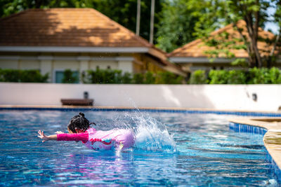 Little girl with pink swim suit jumping into swimming pool in summer.